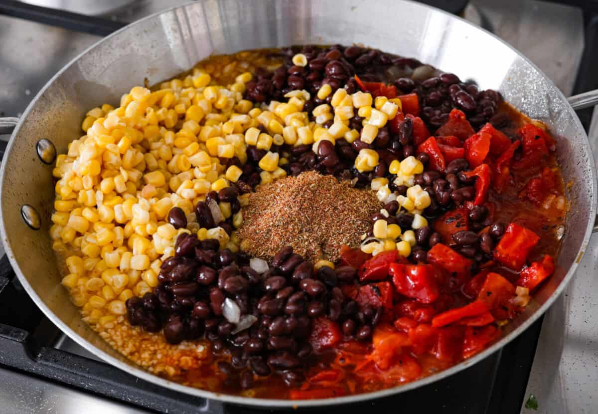 Angle shot of the corn, beans, tomatoes, onions and seasonings all in a pan. 