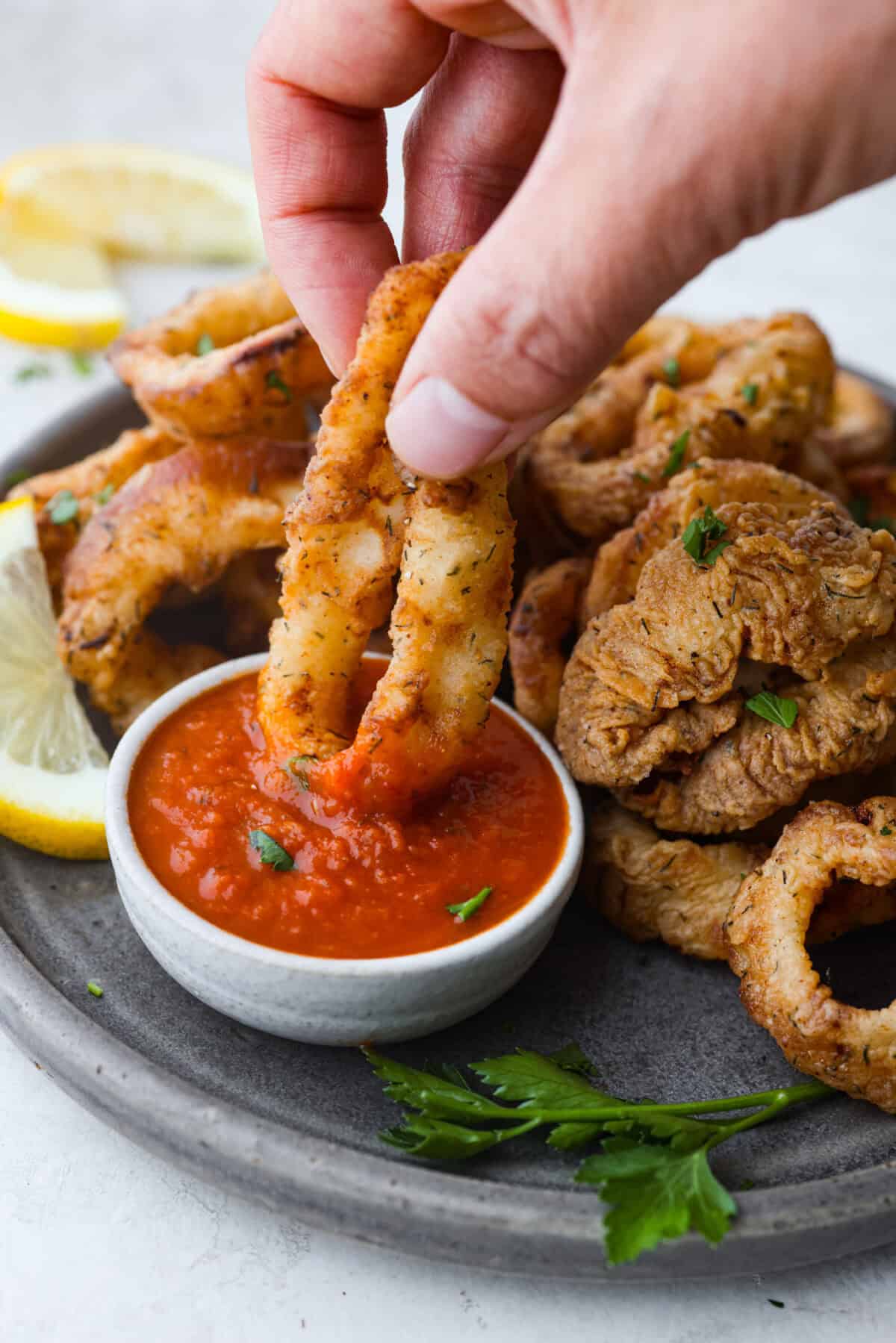 Side shot of someone dipping a fried calamari ring into marinara sauce. 