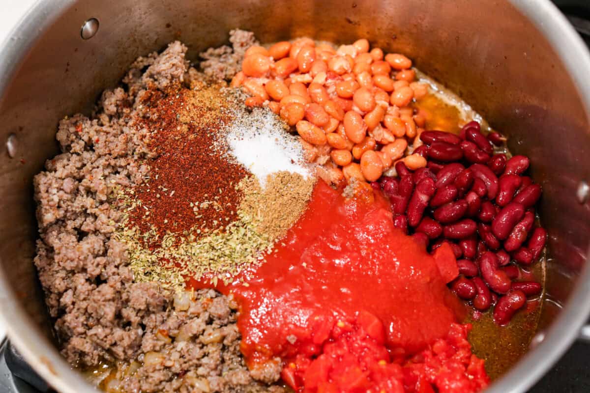 Overhead shot of the beans, seasonings, and tomatoes added to the bacon and sausage. 