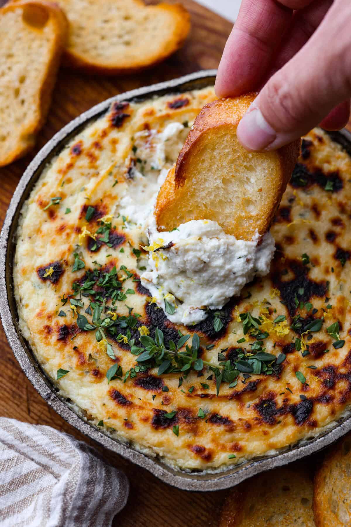 Overhead shot of someone dipping a crostini into the baked ricotta dip.  