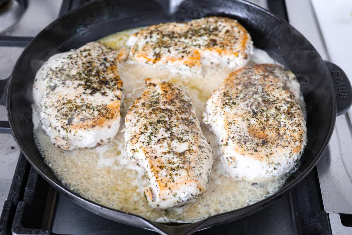 Angle shot of browned chicken breasts in broth and garlic mixture in skillet. 