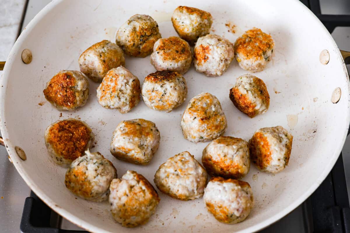 Overhead shot of meatballs browning in a skillet. 