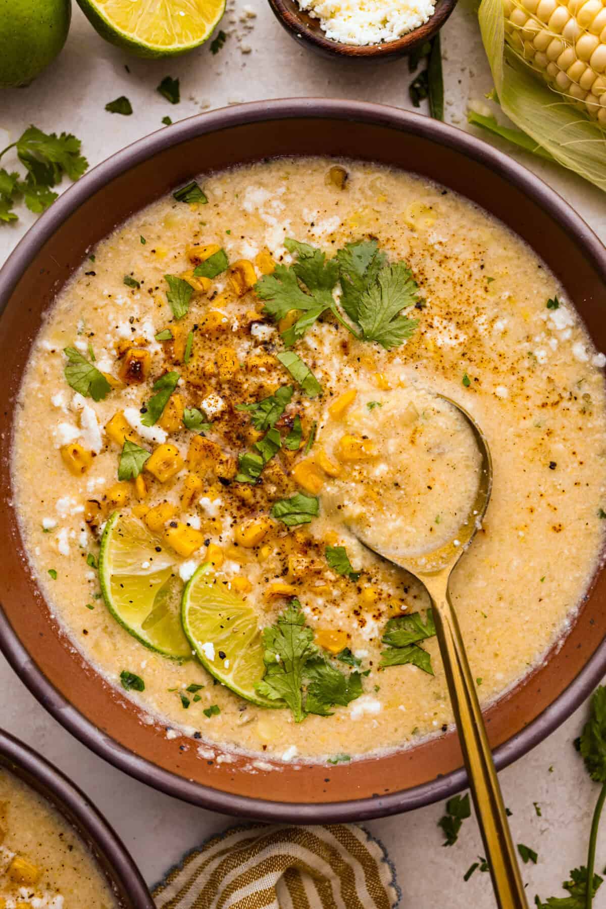 Overhead shot of a bowl of Mexican street corn soup topped with lime wedges, cilantro and cotija cheese. 