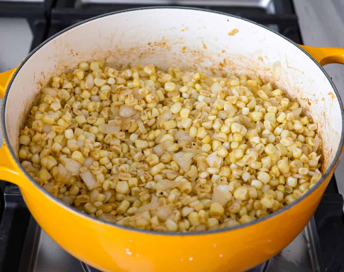 Angle shot of onion and corn in a pot cooking on the stove top. 