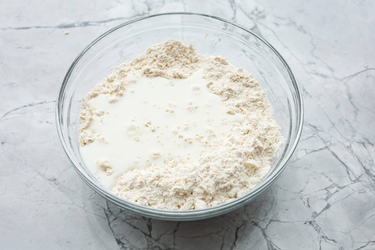 Overhead shot of flour, cream cheese and butt mixture with buttermilk poured over the top. 