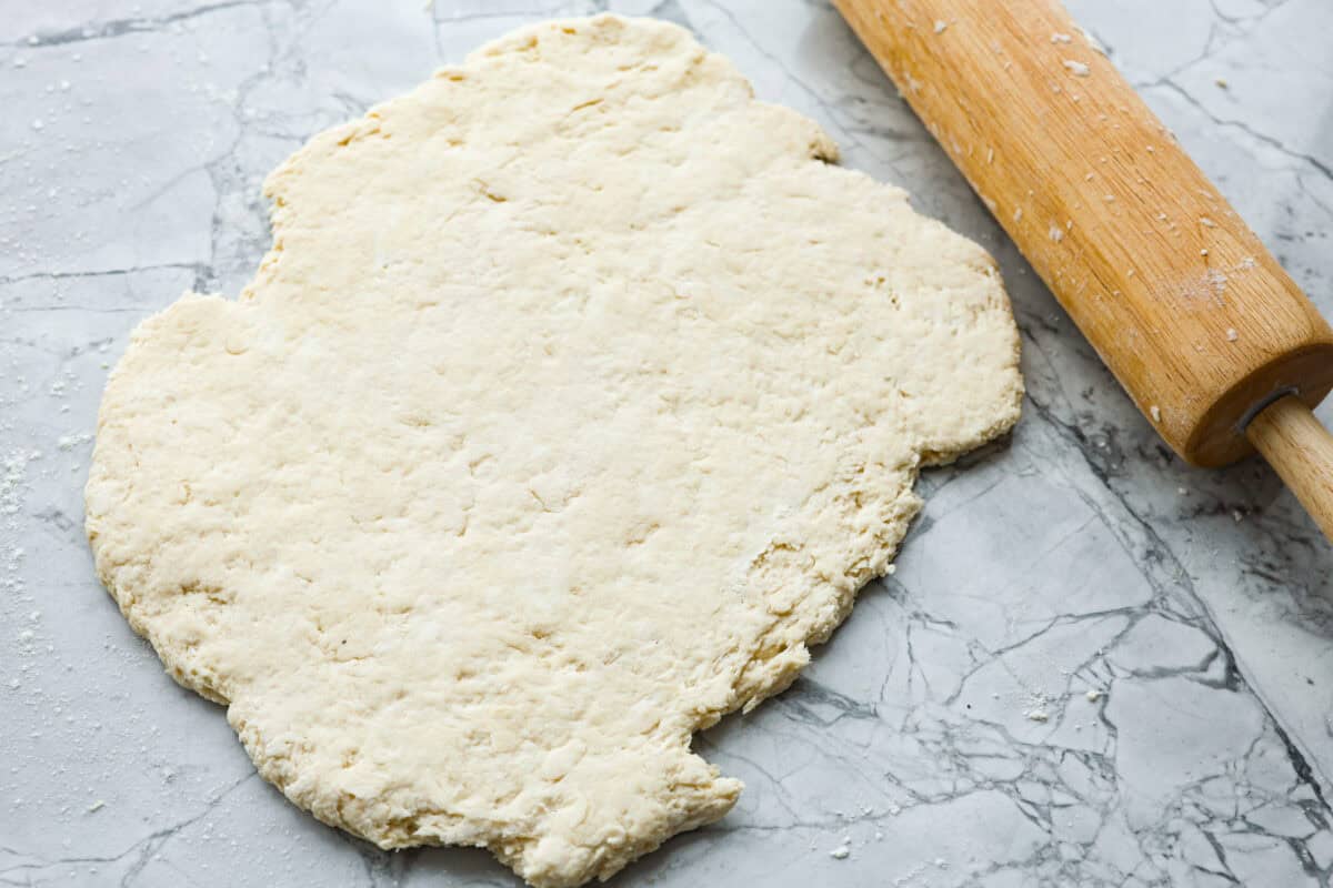 Overhead shot of the cream cheese biscuit dough rolled out next to a rolling pin. 