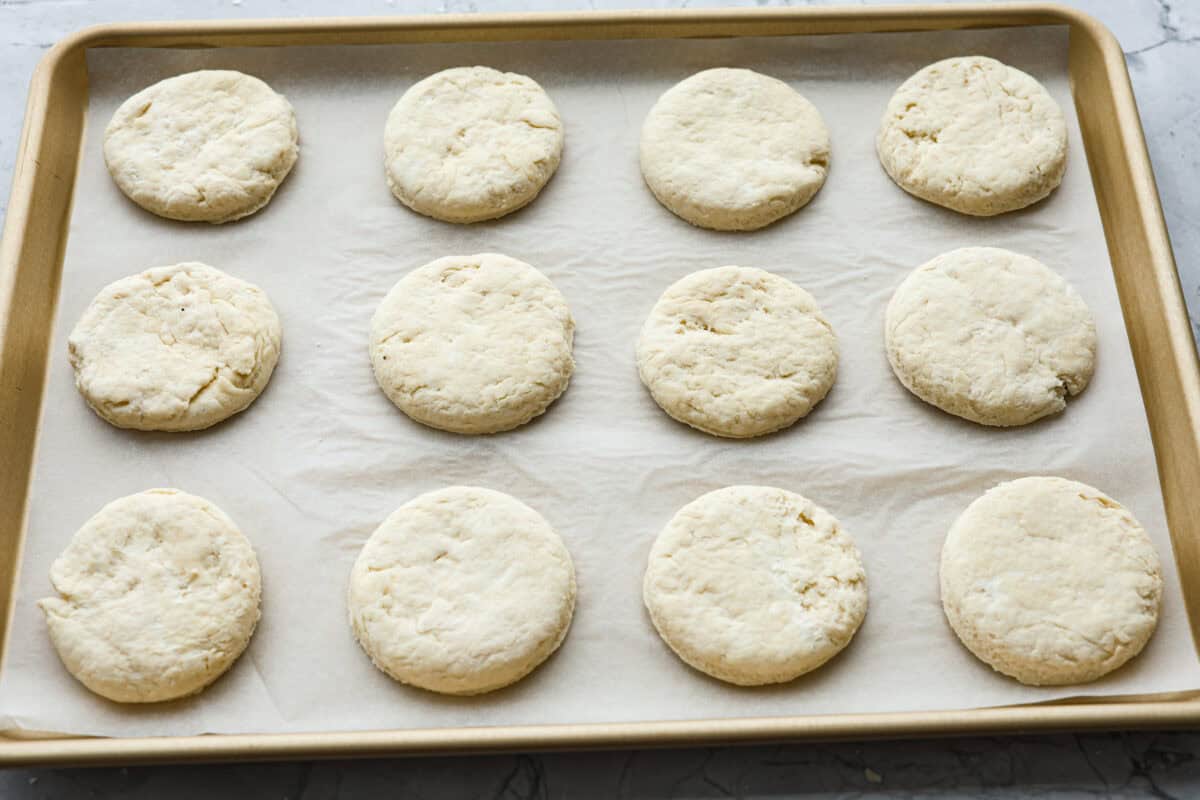 Angle shot of biscuit rounds on parchment paper on a baking sheet.