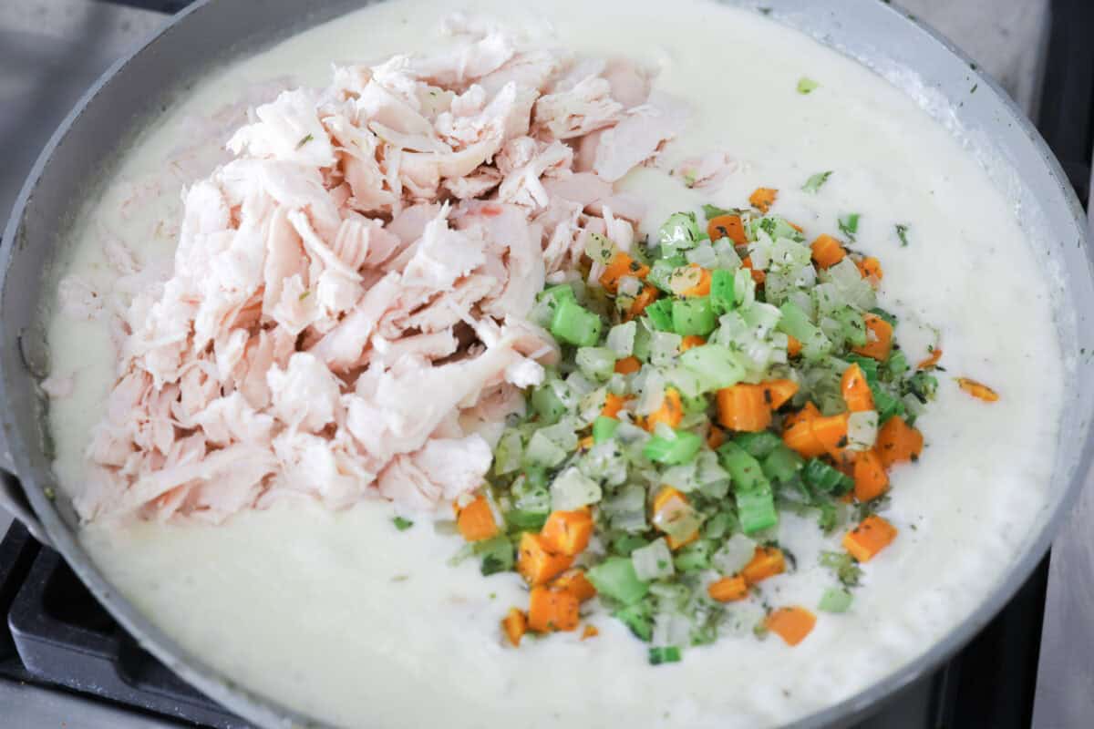 Angle shot of the veggies and chicken being added to the cream sauce in a skillet. 