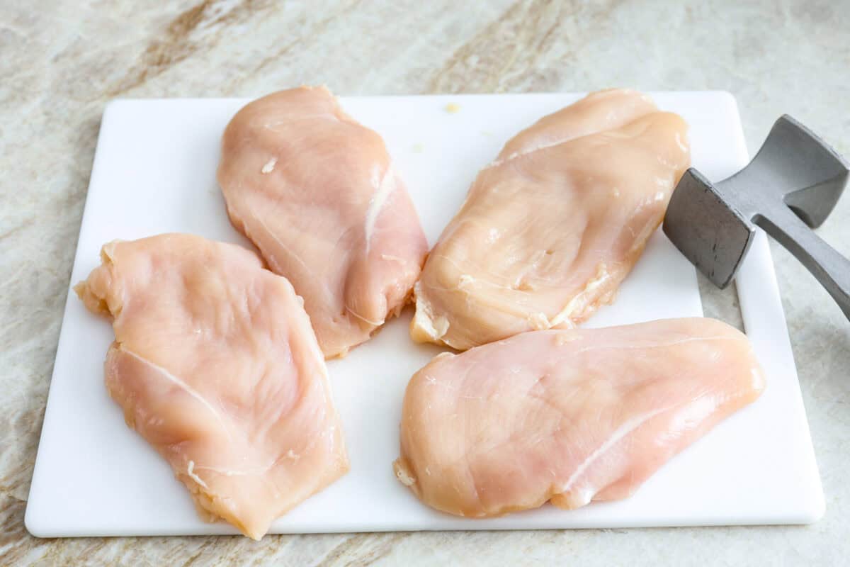 Overhead shot of chicken breasts on a cutting board with meat tenderizer next to them. 