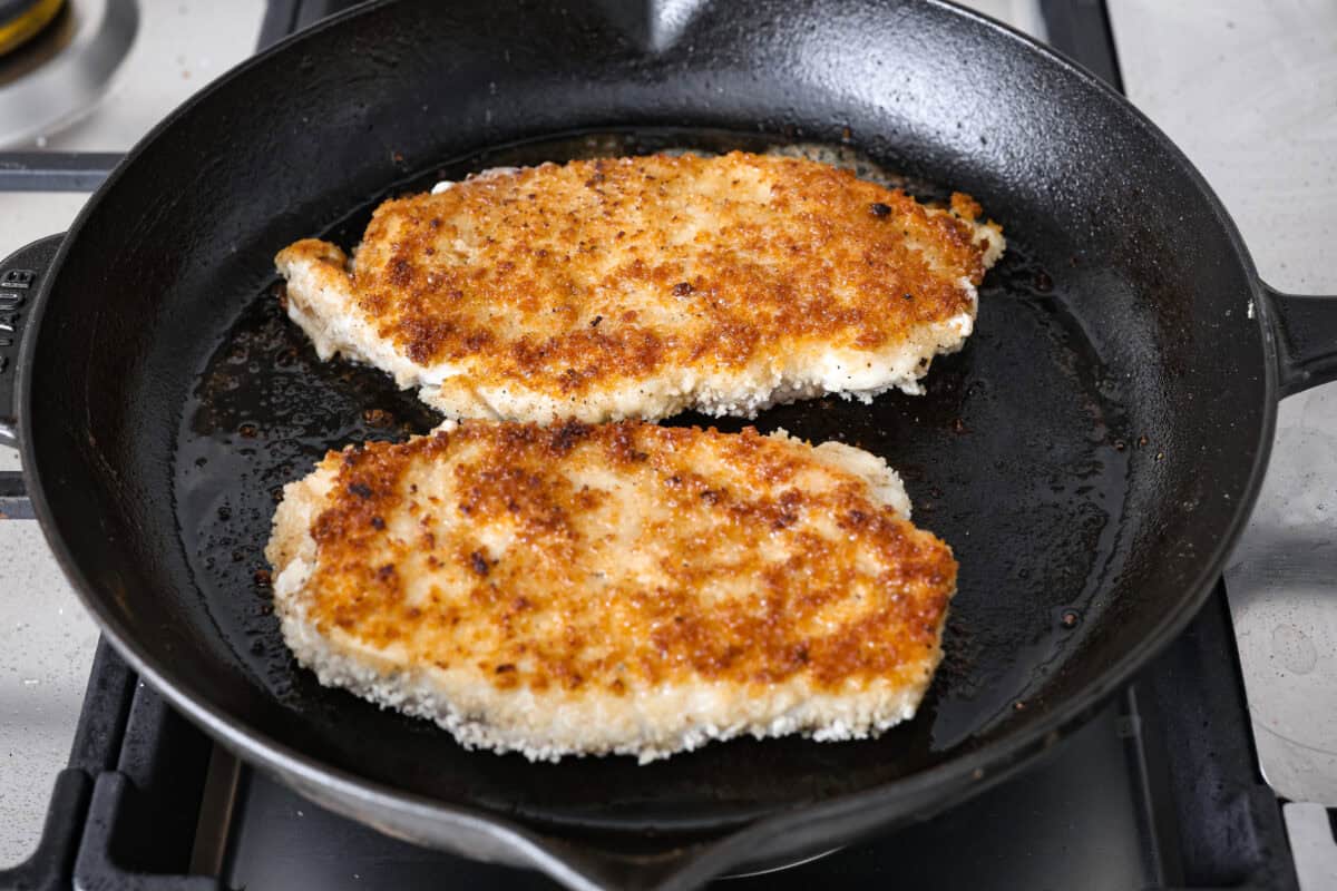 Angle shot of the chicken breast frying in the hot oil in the skillet. 