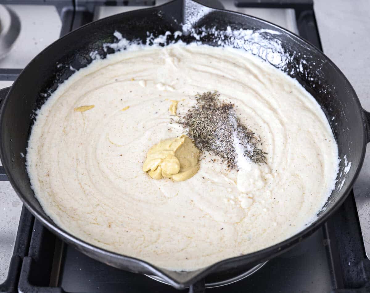 Angle shot of the dijon mustard and seasonings on top of the sauce in the skillet. 