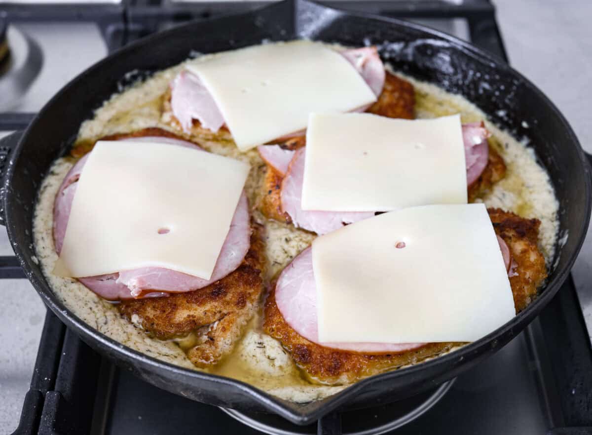 Angle shot of the crispy chicken breasts covered in ham and cheese in the skillet with the sauce. 