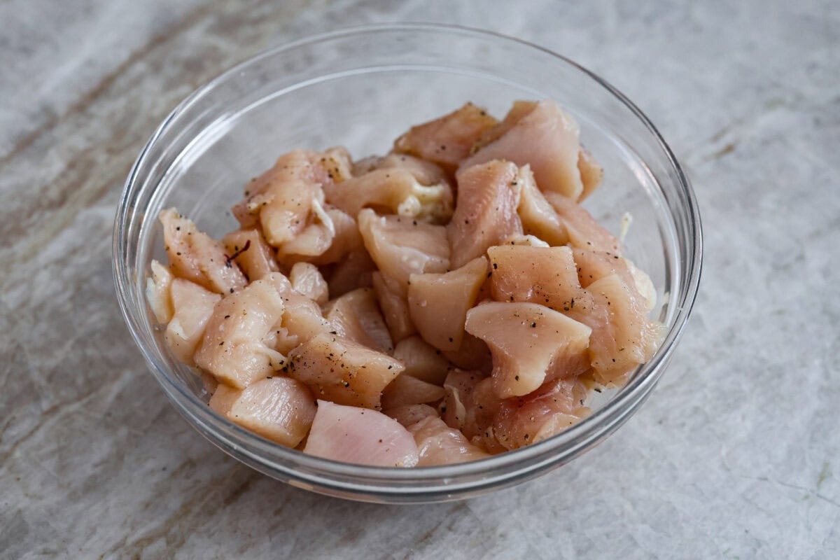 Angle shot of seasoned, cubed  raw chicken in a bowl. 