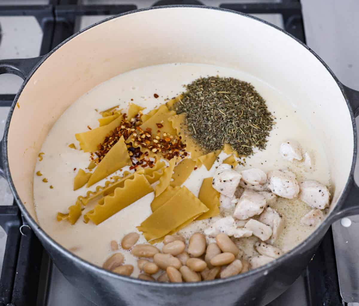 Overhead shot of beans, noodles, seasoning and chicken added to the pot with the soup base. 