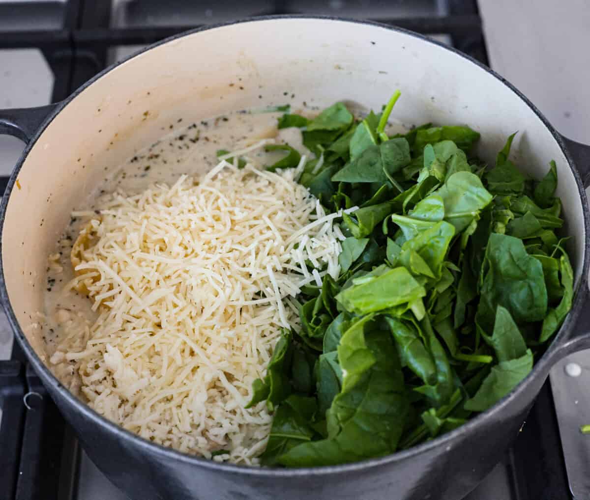 Overhead shot of the cheese and spinach added to the white lasagna soup in a pot. 