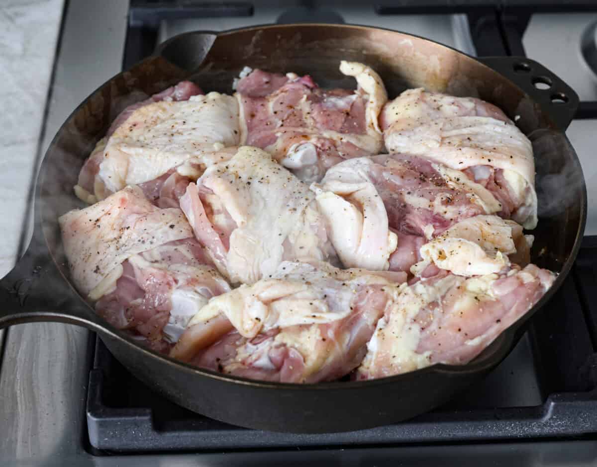 Angle shot of chicken thighs cooking in a skillet. 