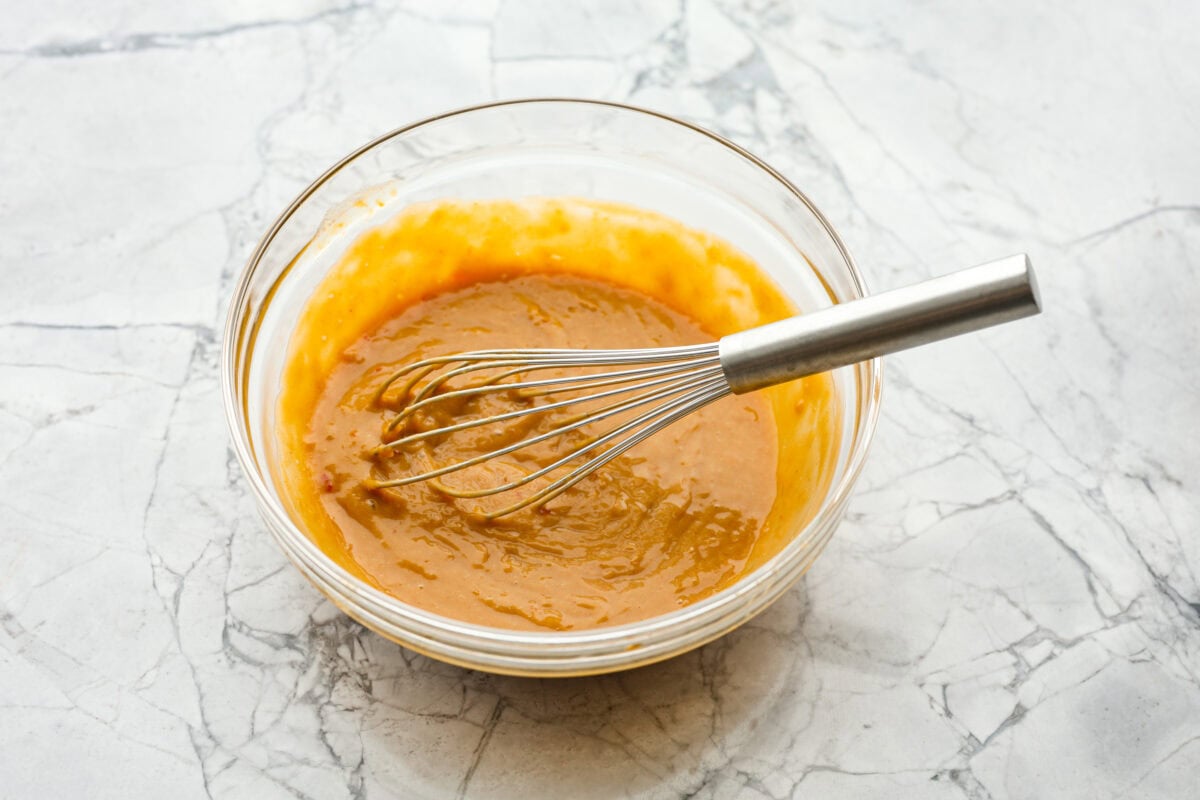 Angle shot of dressing ingredients in a glass bowl with a whisk. 