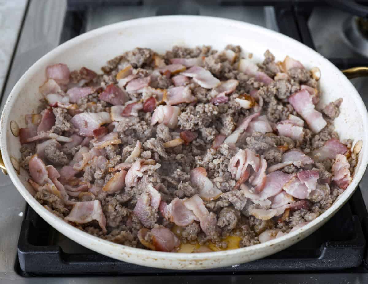 Angle shot of bacon and sausage being cooked in a skillet. 