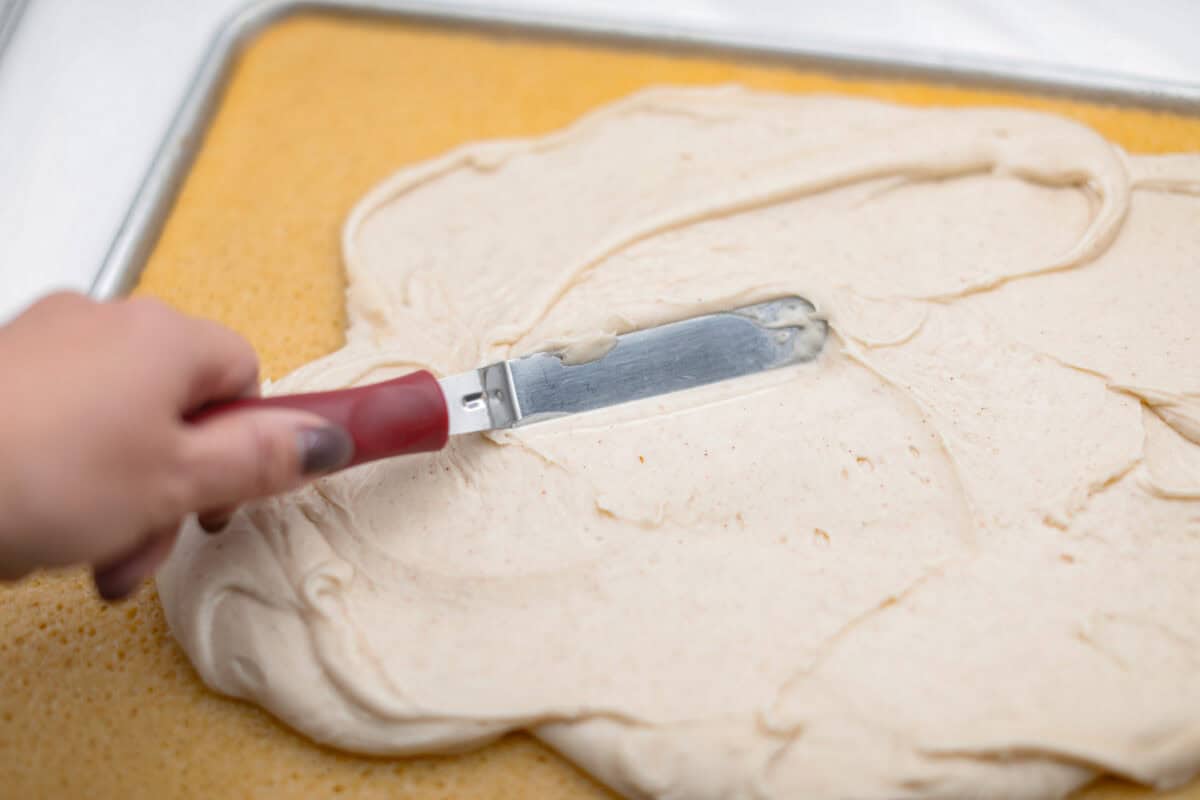 Angle shot of someone spreading the frosting over the cooled sheet cake. 