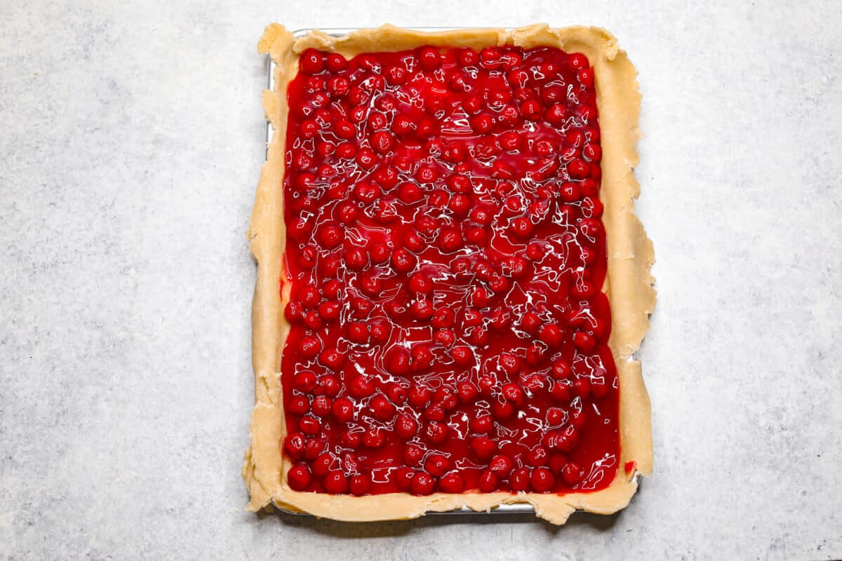 Overhead shot of pie crust on sheet pan filled with cherry pie filling. 