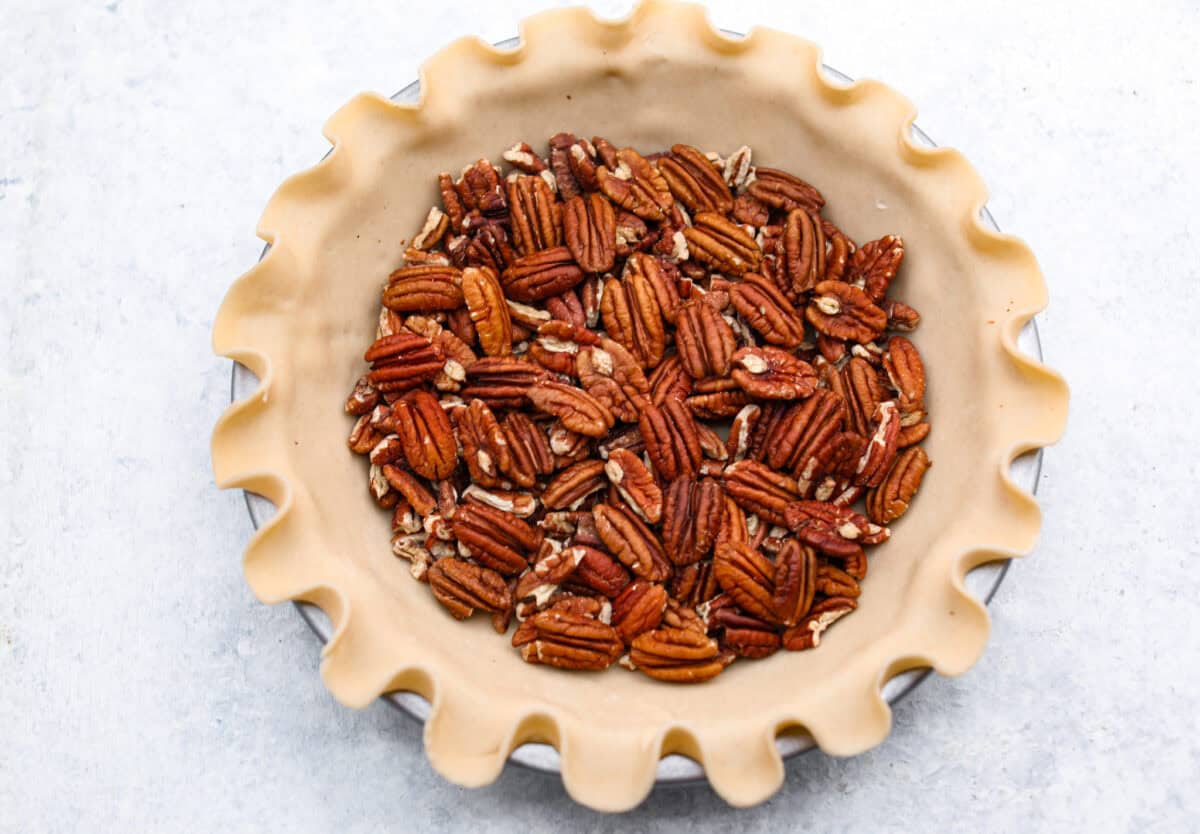 Overhead shot of pecans lining the bottom of a pie crust. 