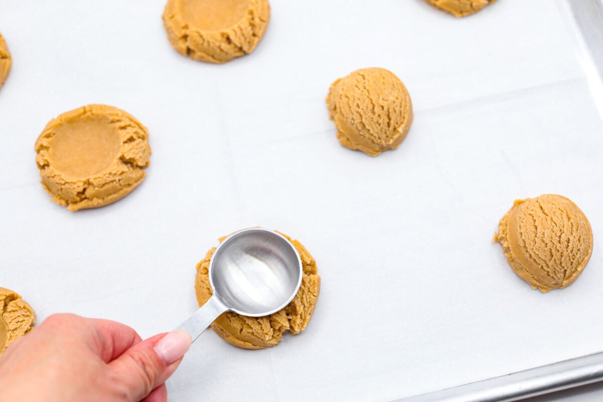 Overhead shot of someone smashing the coffee cake cookie dough balls with the back of a tablespoon. 