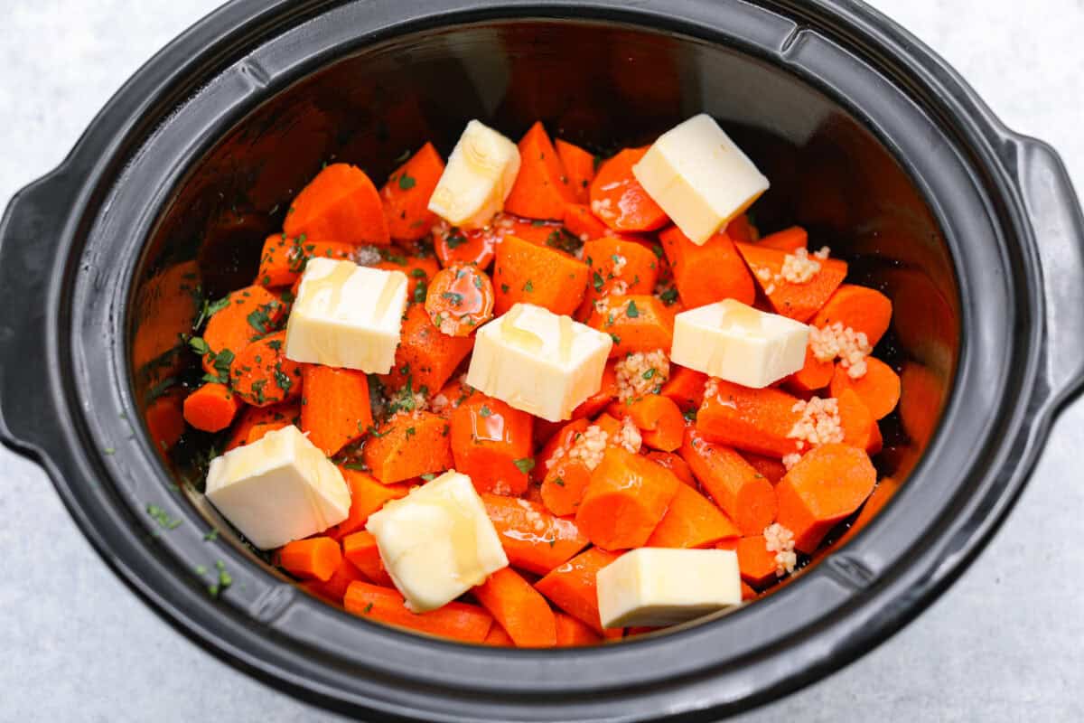 Overhead shot of carrots with honey, butter, garlic, parsley, salt and pepper in a crockpot. 