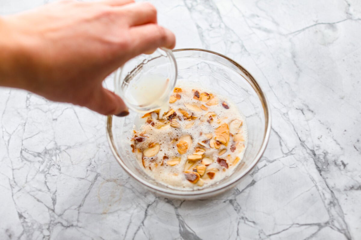 Overhead shot of someone pouring lemon juice into a bowl of the butter and almonds. 