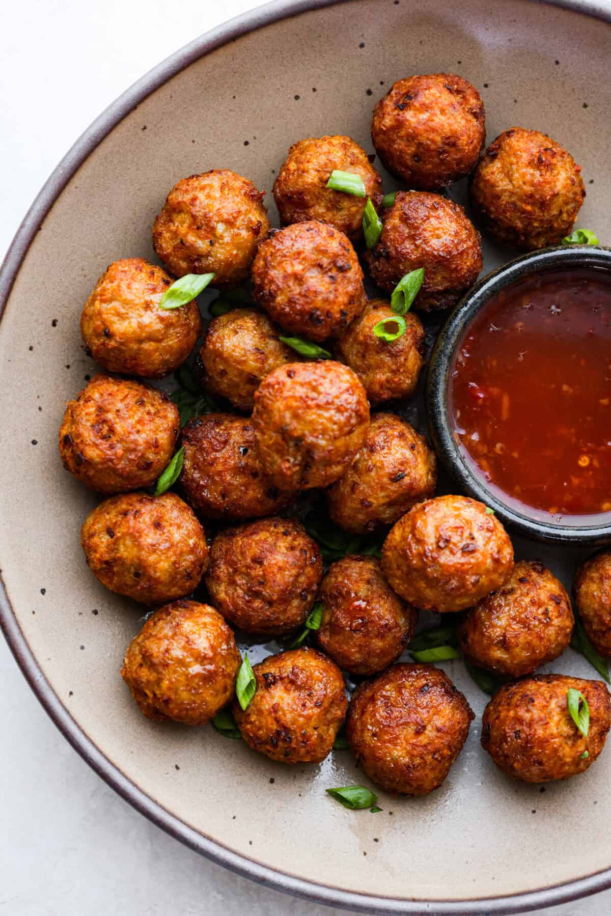 Top view of bola bola filipino meatballs in a bowl with a side of dipping sauce.