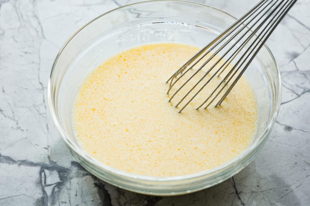 Angle shot of eggs, milk and melted butter whisked together in a bowl. 