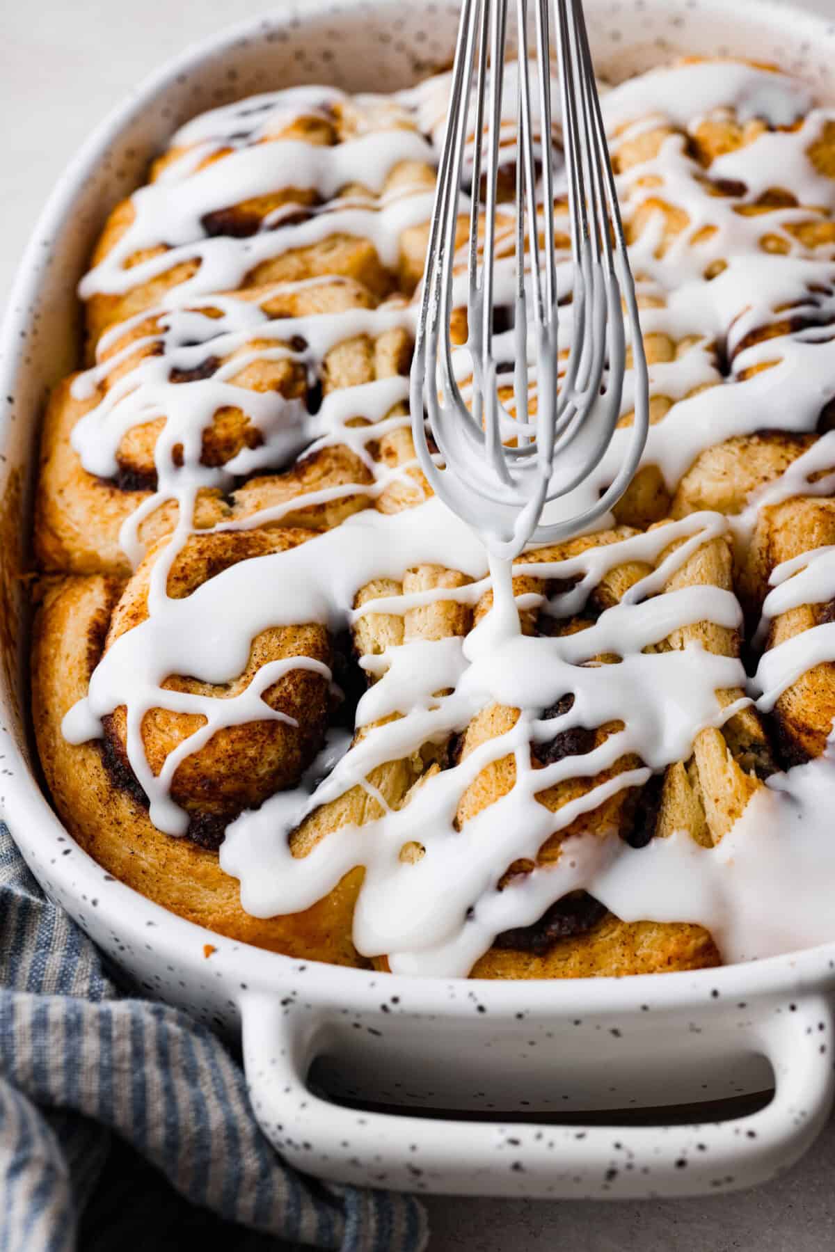 Close up shot of someone drizzling glaze over the biscuit cinnamon rolls. 