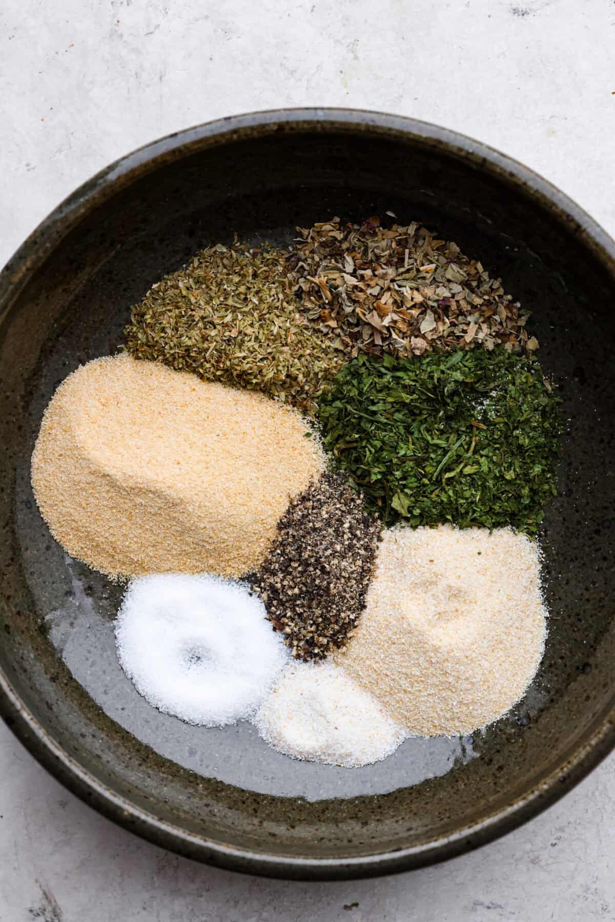 Overhead shot of each ingredient for homemade garlic herb seasoning  in the same bowl in separate piles. 