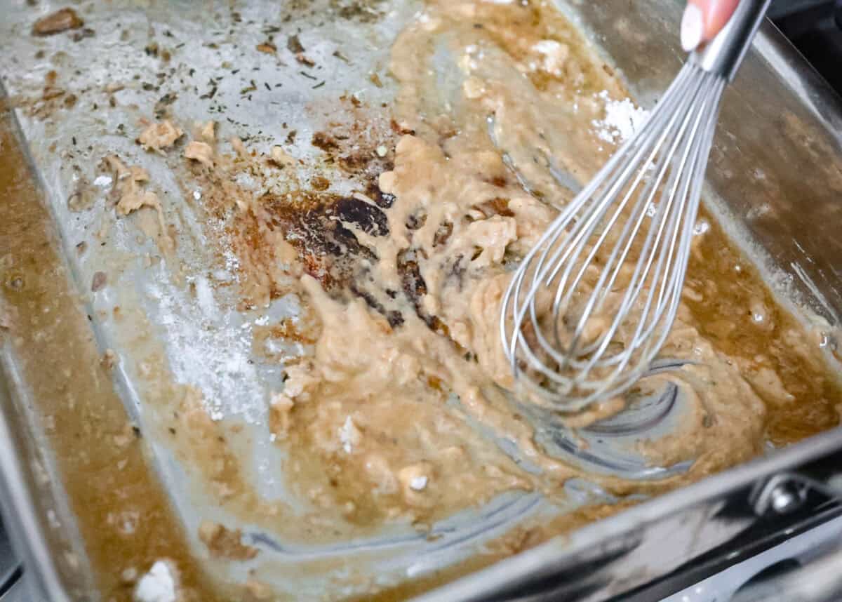 Angle shot of someone whisking flour into the drippings. 