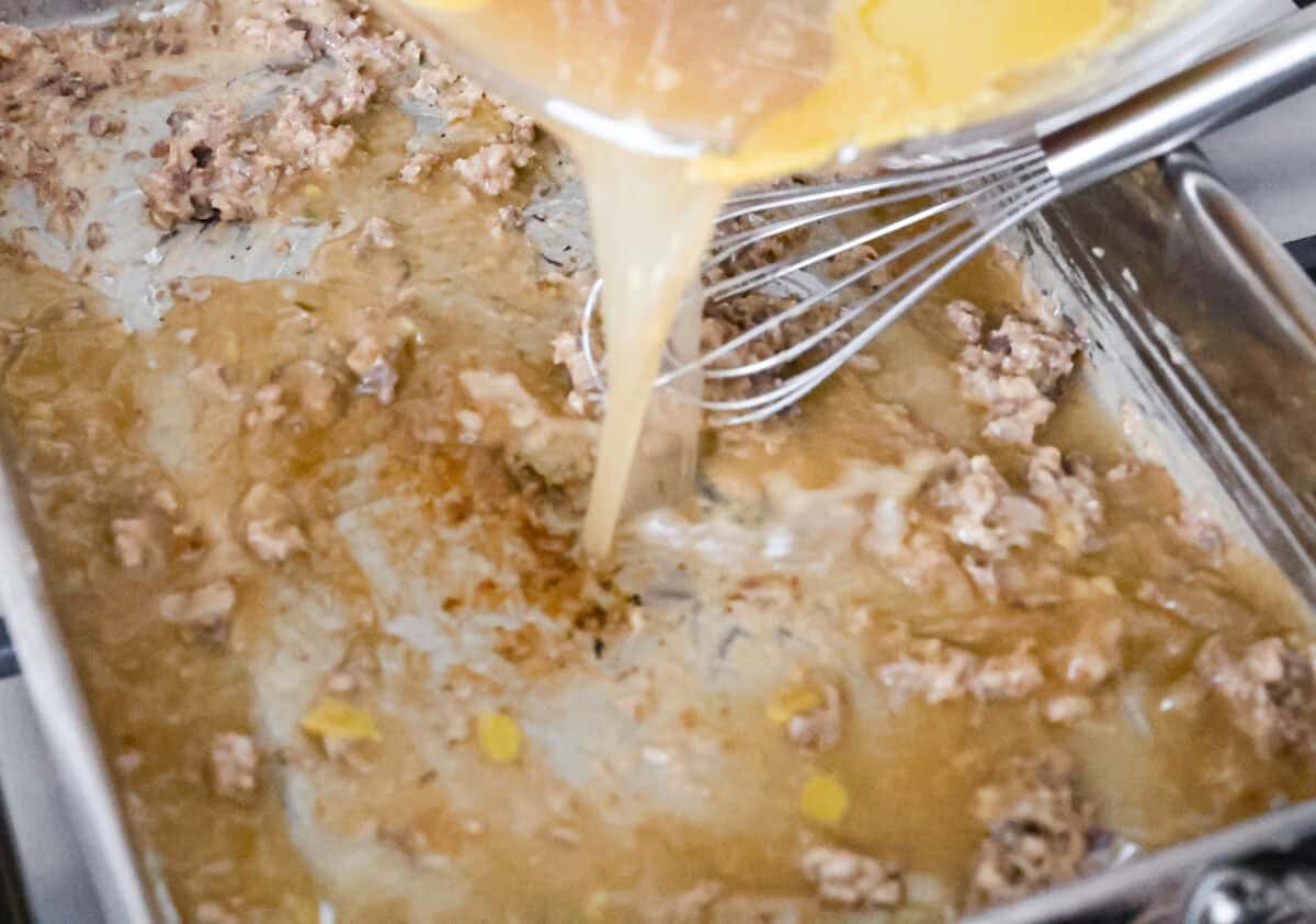 Angle shot of someone pouring the remaining giblet broth into the pan with the giblets, flour and turkey drippings. 