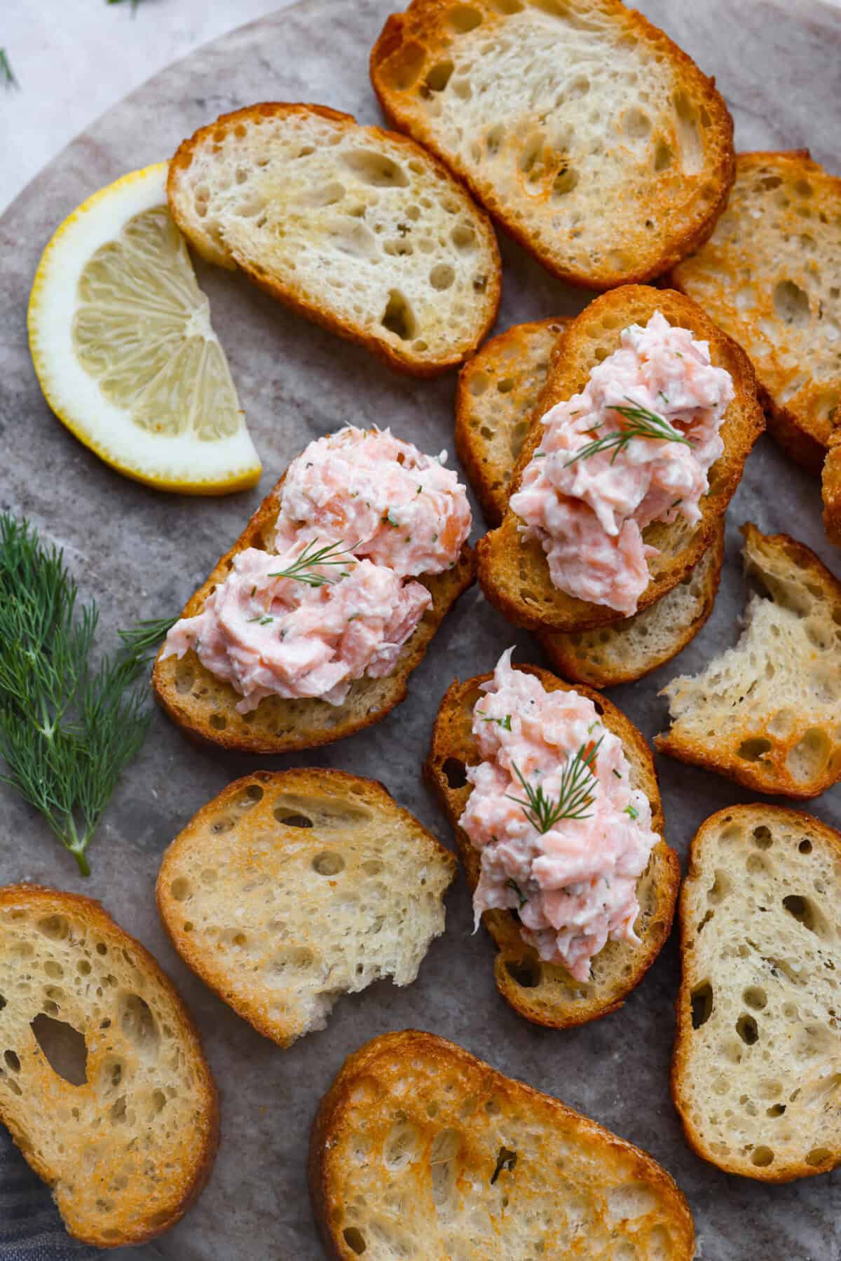 Overhead shot of salmon rillettes on crostini on a serving platter with fresh dill. 