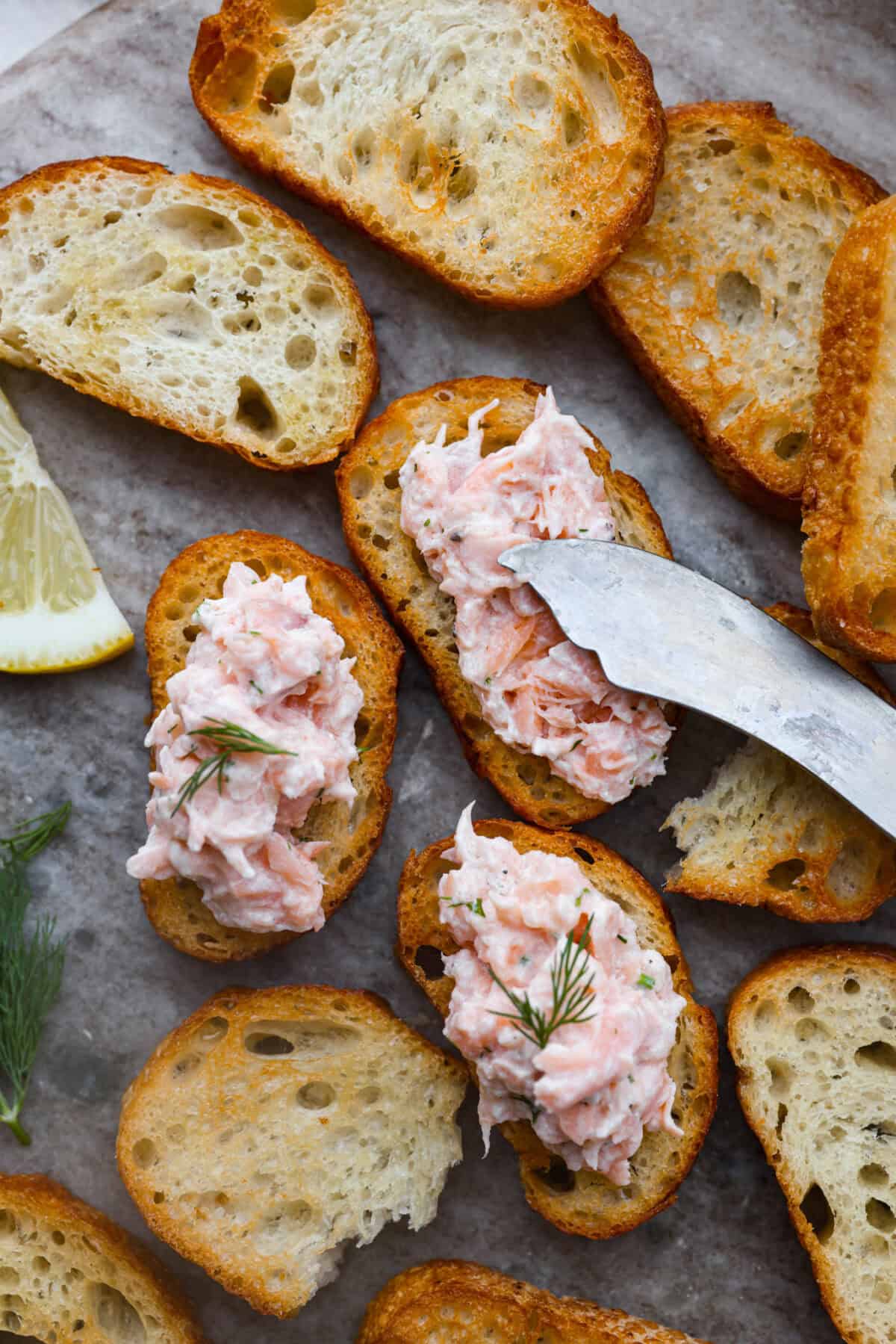 Close up shot of someone spreading salmon rillettes on crostini. 