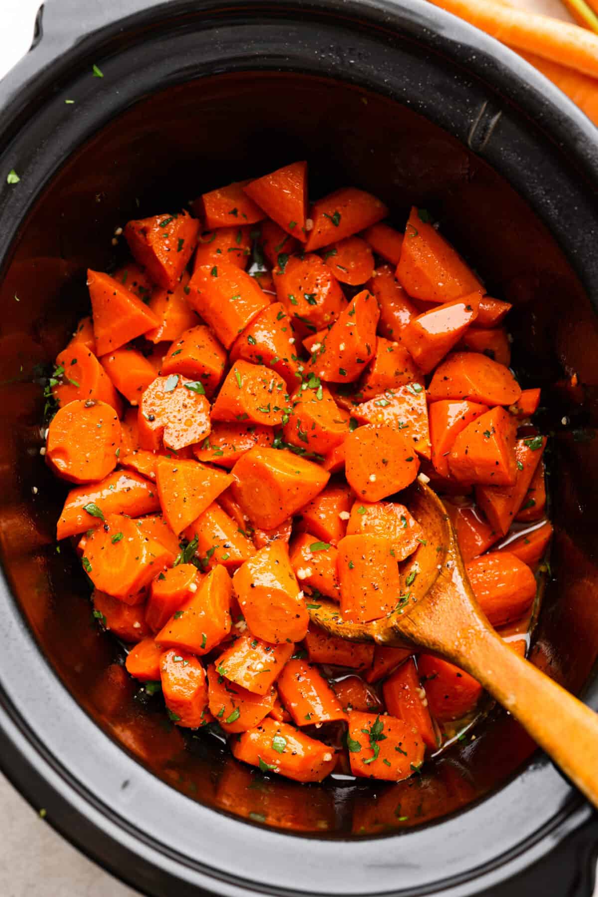 Overhead shot of crockpot carrots in a crockpot with a wooden serving spoon. 