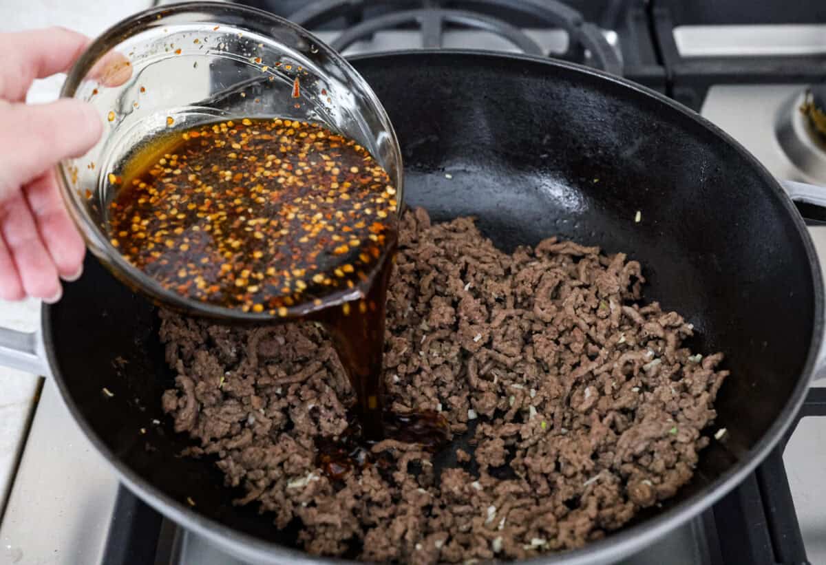 Angle shot of someone pouring the sauce of the drained beef and garlic.  