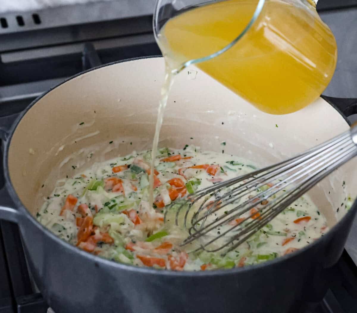 Angle shot of someone pouring chicken broth into the vegetable and flour mixture. 