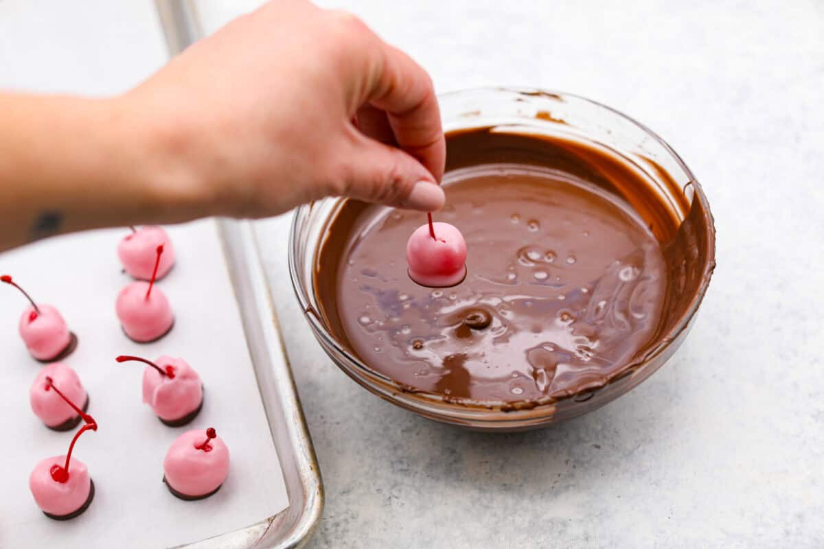 Angle shot of someone dipping fondant dipped cherries into the chocolate. 