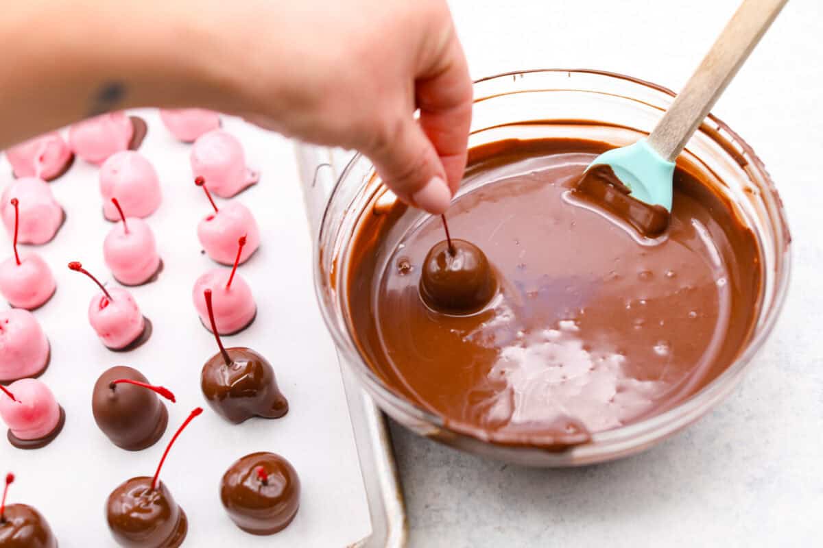 Angle shot of someone holding a chocolate dipped cherry over the bowl of chocolate. 