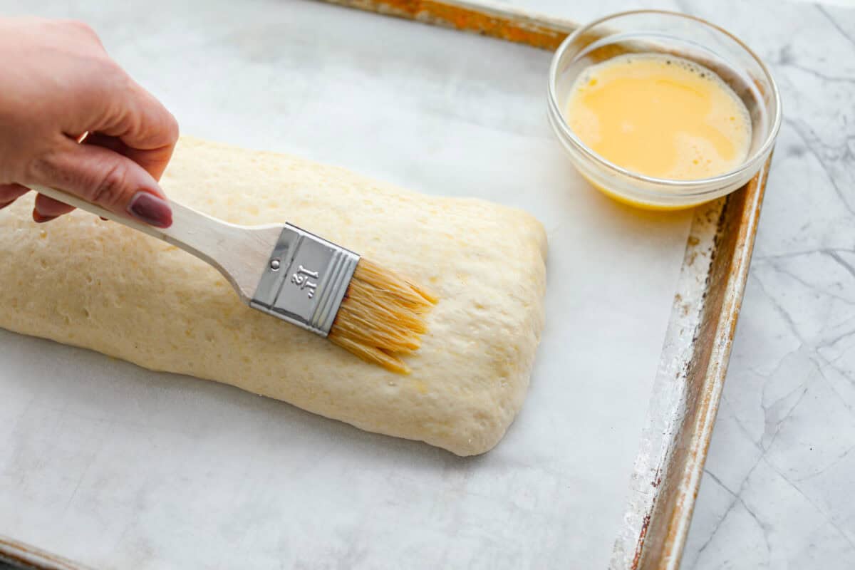 Overhead shot of someone brushing on an egg was over the flipped sealed pizza dough. 