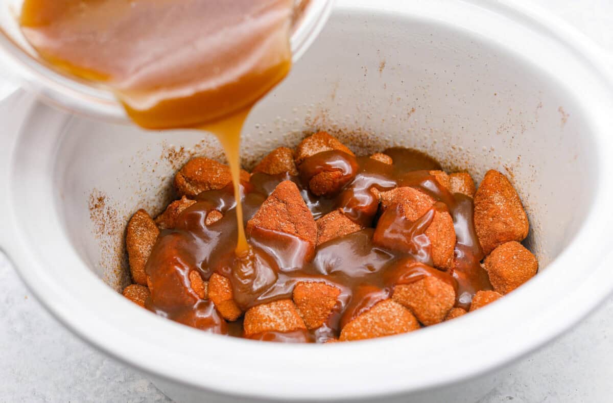 Angle shot of someone pouring brown sugar and butter glaze over the top of the biscuits. 