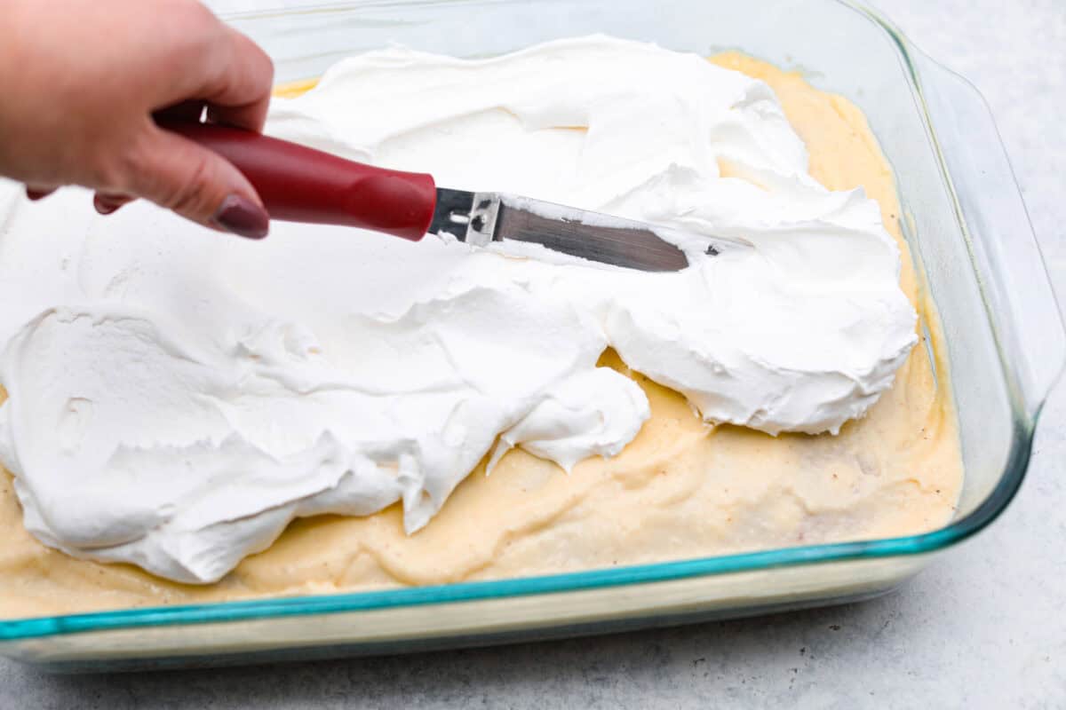 Angle shot of someone spreading whipped topping over the spread topping. 