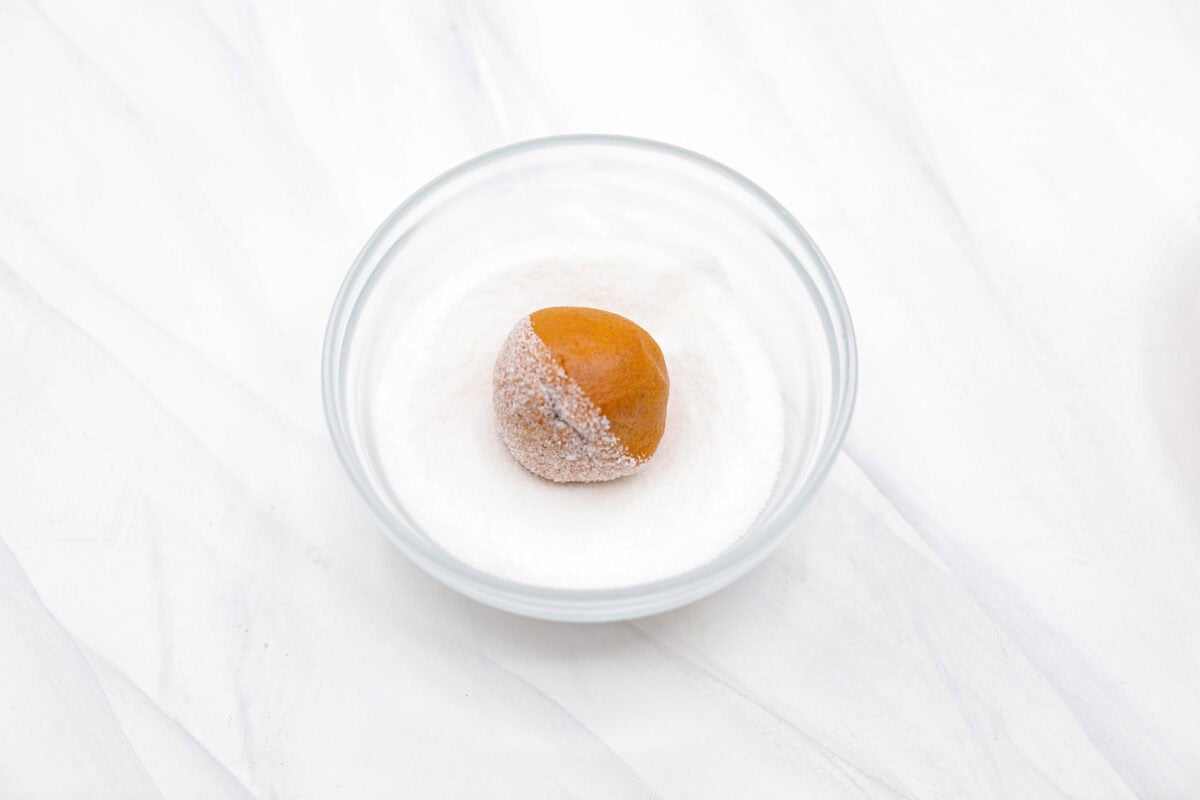 Angle shot of gingerbread crinkle cookie dough ball in a bowl of granulated sugar.