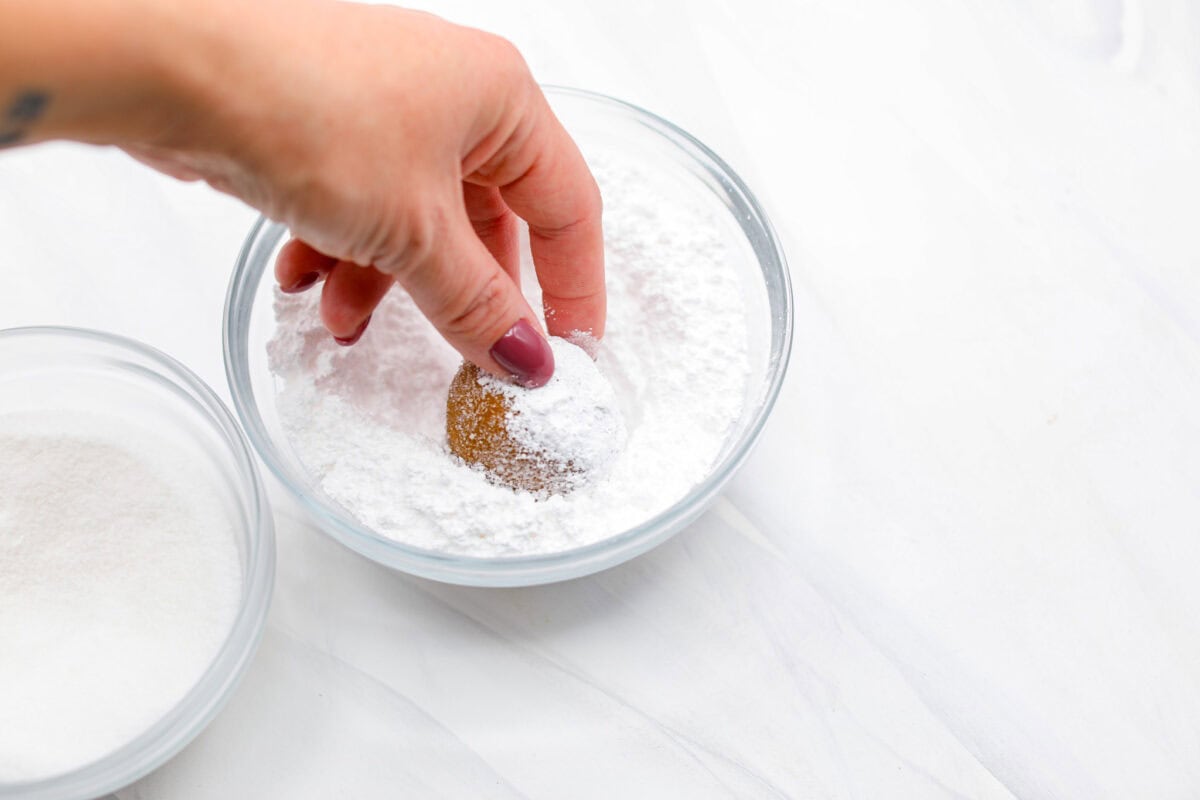 Angle shot of someone rolling a dough ball in powdered sugar.