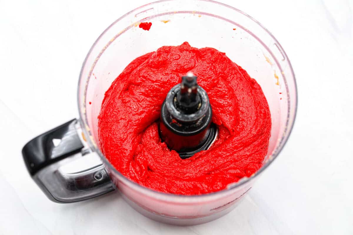 Overhead shot of cookie crumbs, cream cheese and red food coloring mixed together in a food processor. 