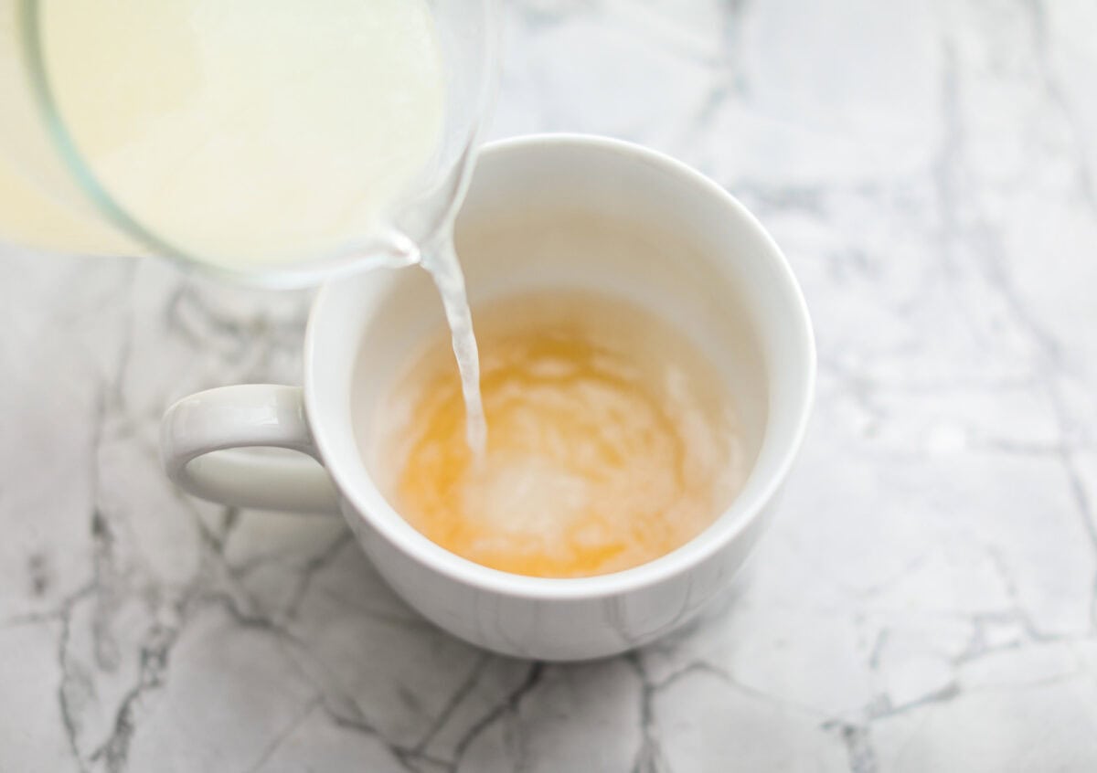 Overhead shot of someone pouring the hot lemonade into the mug with the honey. 