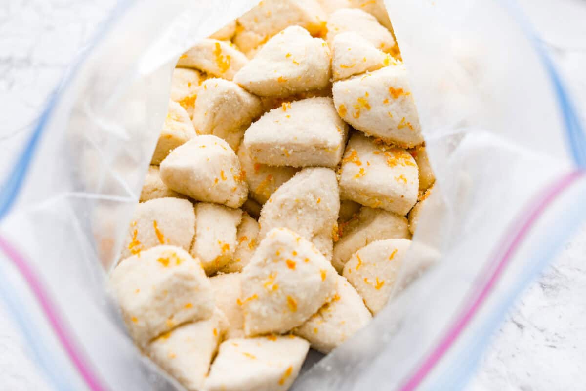 Overhead shot of biscuit quarters in a ziplock back mixed with sugar and orange zest. 