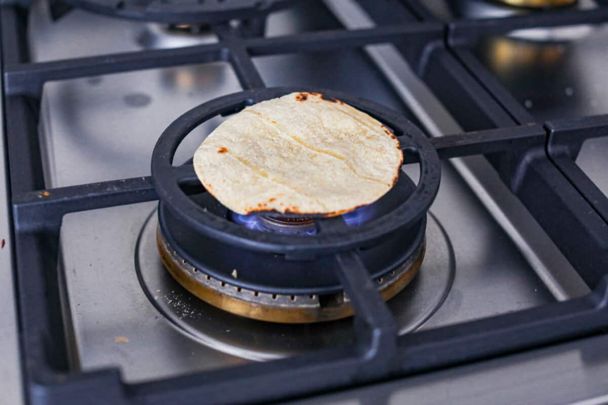 Angle shot of a corn tortilla straight on a gas burner. 